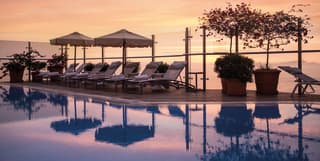 Hotel infinity pool surrounded by potted plants and sunbeds at sunset