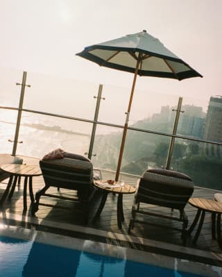 Angled image across the rooftop pool to a deck with two loungers beneath a parasol, overlooking Lima's incredible coastline.