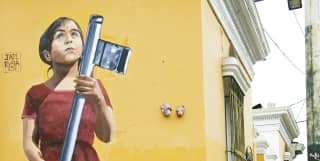 A woman looking at her phone, leaning against a yellow wall in Barranco, Lima