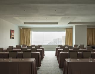 A wide Salón Pacifico window reveals the venue's incredible coast views, seen over eight brown-clothed tables with chairs.