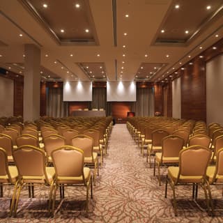 Rows of coral-hued banquet chairs in a large venue with a pink patterned carpet