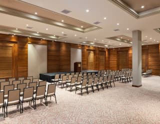 Chairs, grouped in columns, face the stage in the Copacabana meeting room, lit with glowing spotlights, seen from behind.