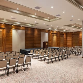 Chairs, grouped in columns, face the stage in the Copacabana meeting room, lit with glowing spotlights, seen from behind.