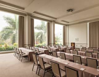 Three tall windows spill light into Salón Park, where ten long beige tables, each seating four chairs, face the front.