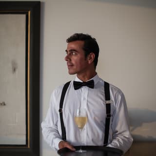 Sommelier wearing a black bow-tie and white shirt, carrying a glass of white wine