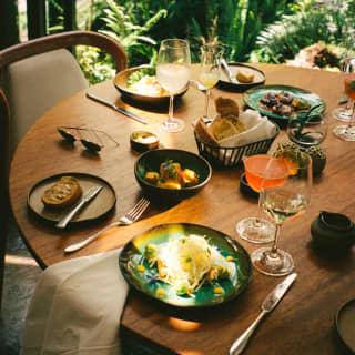 A beam of sun glances over plates of vibrant food at a table with wine and cocktails at Tampu Restaurant, seen from above.