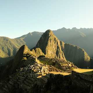 Sunshine illuminates the ancient ruins of Machu Picchu, cradled between the verdant peaks of Huchuy Picchu and Huayna Picchu.