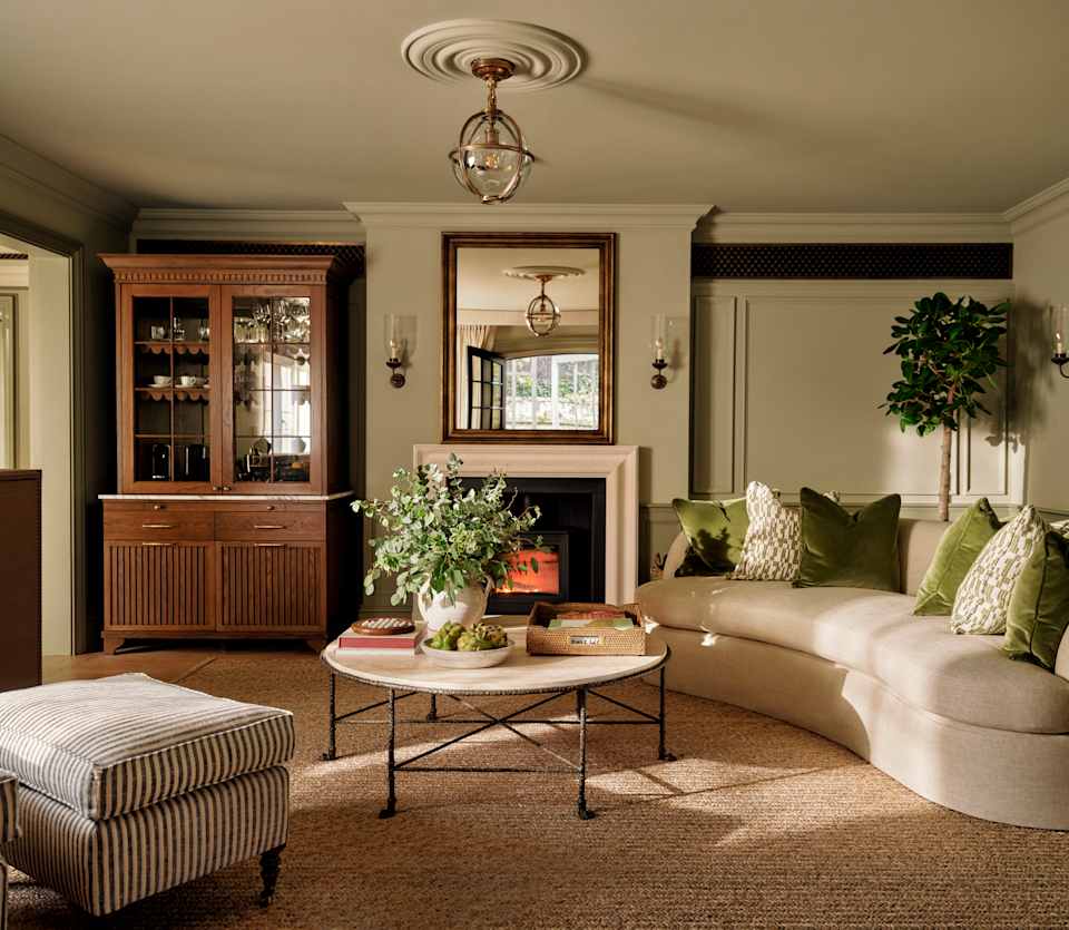 View over the Artichoke Suite living room with round table, footstool and beige kidney sofa with furnishings in green hues.