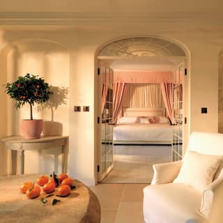 Two kumquat trees in terracotta pots stand on half moon tables in arched nooks flanking a doorway to a sumptuous bedroom