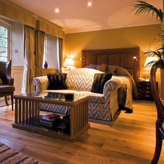 Oak flooring offers a natural warmth, along with leather chairs and wooden coffee table. A padded headboard frames the bed