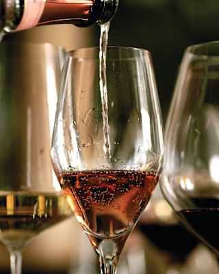 Rosé champagne being poured into a glass with red and white wine either side