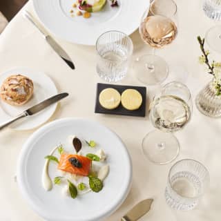 A birds eye view of a round table for two, set with a white table cloth and serving starters with a glass of white and rose