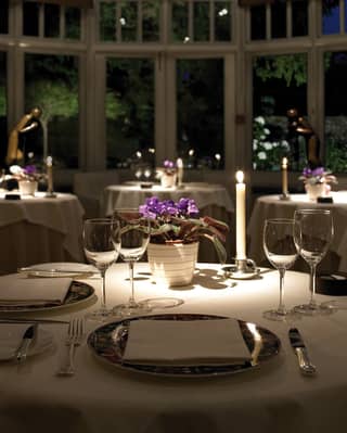 Single candles and potted African violets on each table add a romantic feel to a charming conservatory restaurant at night