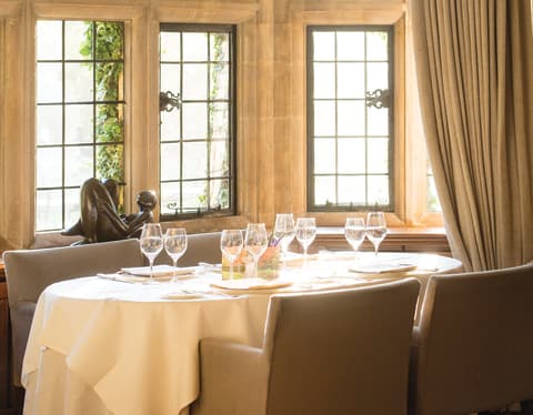 A table set for four occupies the bay of a stone mullioned window nook. A small bronze figure sits on the window sill
