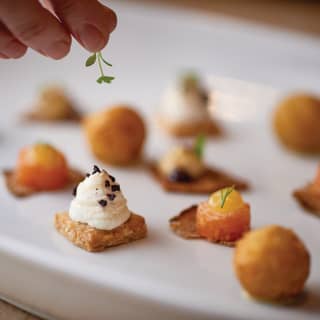 A chef carefully places a sprig of leafy garnish to a plate of colourful and enticing canapés arranged on a white plate
