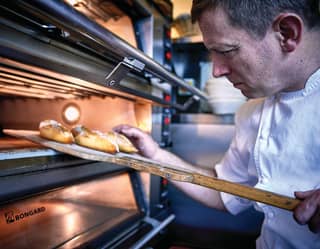 Acclaimed chef, Benoit Blin, checks the texture of freshly cooked pastries as he uses a wooden pizza paddle to remove them