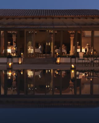Candlelit restaurant at night with an open terrace reflected in a pool below