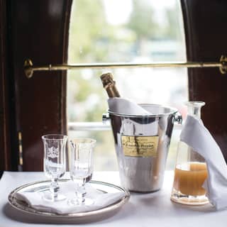 Two champagne flutes sit on a silver salver. A bottle of champagne is in an ice bucket and orange juice in a glass carafe