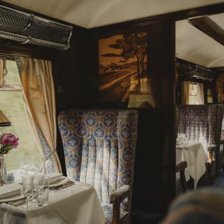 In Audrey, a luxurious blue-grey seat faces a table and abuts a partition wall with a marquetry depiction of a country scene.