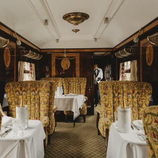 A steward approaches the Ibis Car where Champagne bottles await guests on three visible tables with seats in warm gold tones.