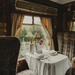 A window spills light on to a table set for two with a lamp, flower and Champagne, flanked by Ione's taupe-patterned chairs.