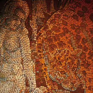 A detailed mosaic in tiny tiles of sunset oranges and reds depicts the Greek goddess, Rhea, holding her open palm to lioness