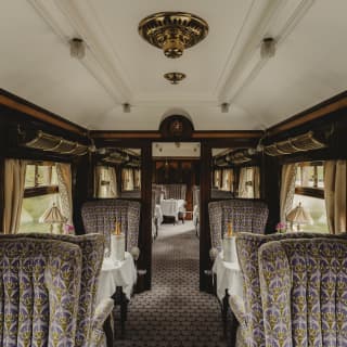 Dining chairs in a rich purple and gold fabric flank tables set for two with Champagne coolers, in a view of the Minerva Car.
