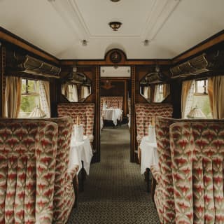 View through the Zena Car with dining tables and seats, upholstered in a grey and pink fabric, and wood panelled walls.