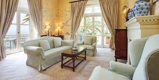Double-height hotel suite lounge area with yellow floral wallpaper and large fireplace