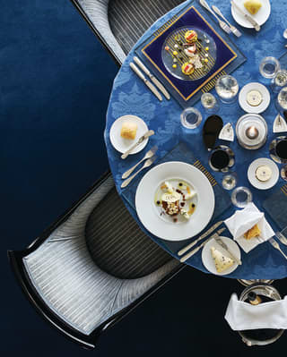 Circular table topped with a blue-patterned tablecloth and formal dinner settings