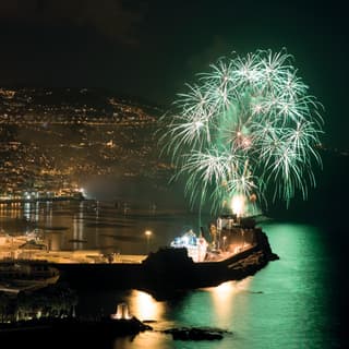 White and green star-cluster fireworks light up the night sky above Funchal marina, casting a peppermint hue on the water.