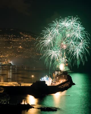 White and green star-cluster fireworks light up the night sky above Funchal marina, casting a peppermint hue on the water.