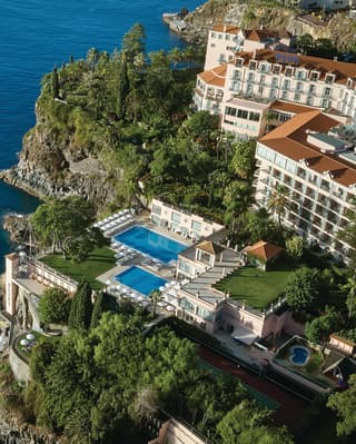 Aerial view of a large hotel building on a lush garden cliff top overlooking the sea