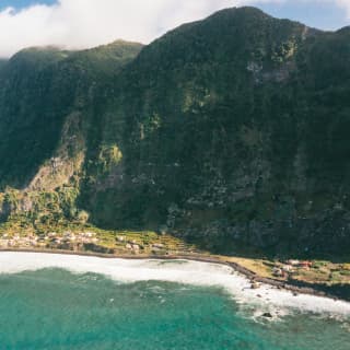 Steep hills drop dramatically into verdant, narrow coastal plains bordering the dramatic coastline of Sao Jorge island.