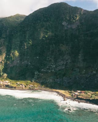 Steep hills drop dramatically into verdant, narrow coastal plains bordering the dramatic coastline of Sao Jorge island.