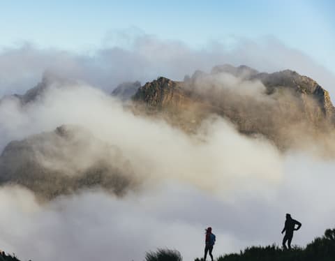 The silhouettes of two hikers on the Levada da Negra stop to view the incredible cloud-shrouded ridge of Pico do Arieiro.
