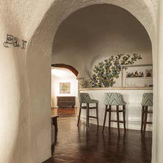 View through a white-rendered internal doorway into an area where three grey, high-back stools line a curved white bar.