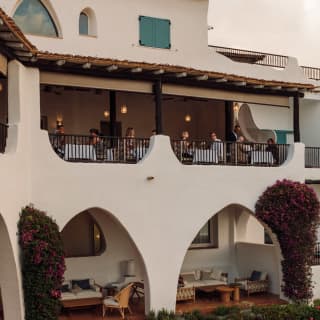 Three couples dine on the softly-lit terrace at La Terrasse restaurant as evening falls, seen from lawn garden below.