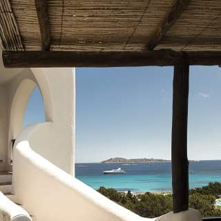A tiled external staircase with curved stucco walls sweeps up to a terrace, offering interim views of dazzling blue sea.