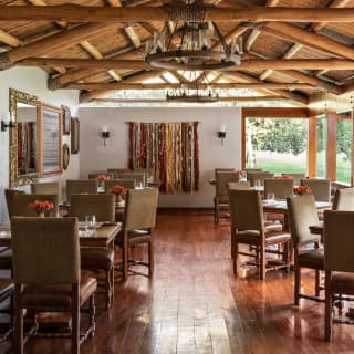 View through El Huerto's interior with two rows of tables and chairs in natural hues, solid wood floors and beamed ceiling.