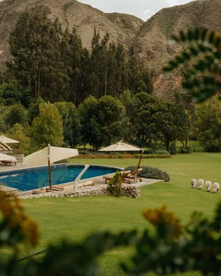 Dramatic hills rise behind the Rio Sagrado pool, edged by loungers and parasols, which sits like a sapphire in emerald lawn.