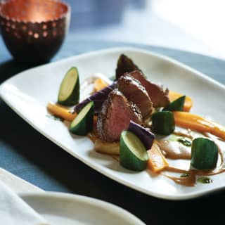 A white plate of beautifully presented meat and vegetables on a restaurant table