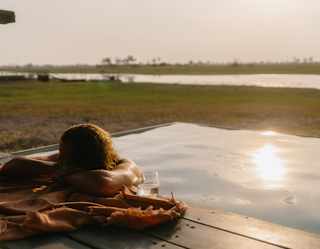 Eye-level view of a man in the pool with his head resting on his arms on the edge, with a towel and glass of water.