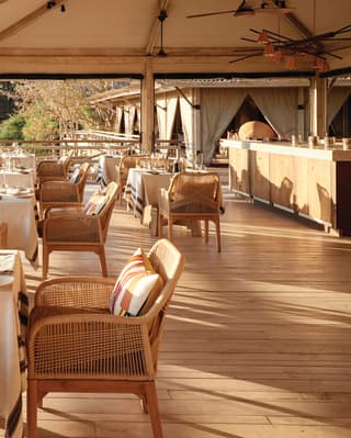 Dining tables and cane chairs under a canopy on the decking overlooking the savannah