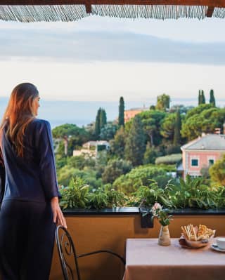 Lady in a navy dress leaning on a balcony wall overlooking Mediterranean gardens