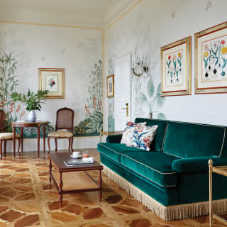 Gold tassels fringe the base of an elegant green velvet sofa. Framed botanical art fills the walls, beside large botanical murals