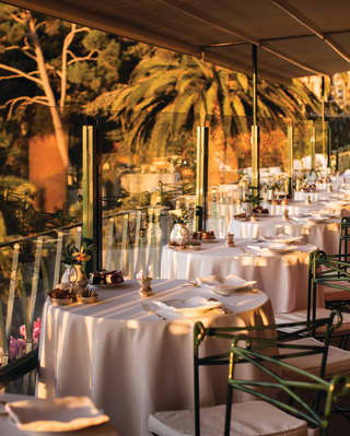 Formal linen-coated circular dining tables in a row on a restaurant terrace at sunset