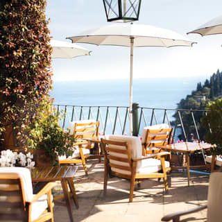 Sun-splashed, sea view restaurant terrace with coffee tables under white parasols
