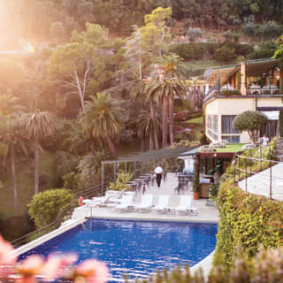 Hotel pool set among stunning Mediterranean gardens beneath a hilltop villa
