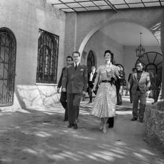 A black and white 1950s image of Ava Gardner as she walks out of the hotel surrounded by an entourage of men in suits